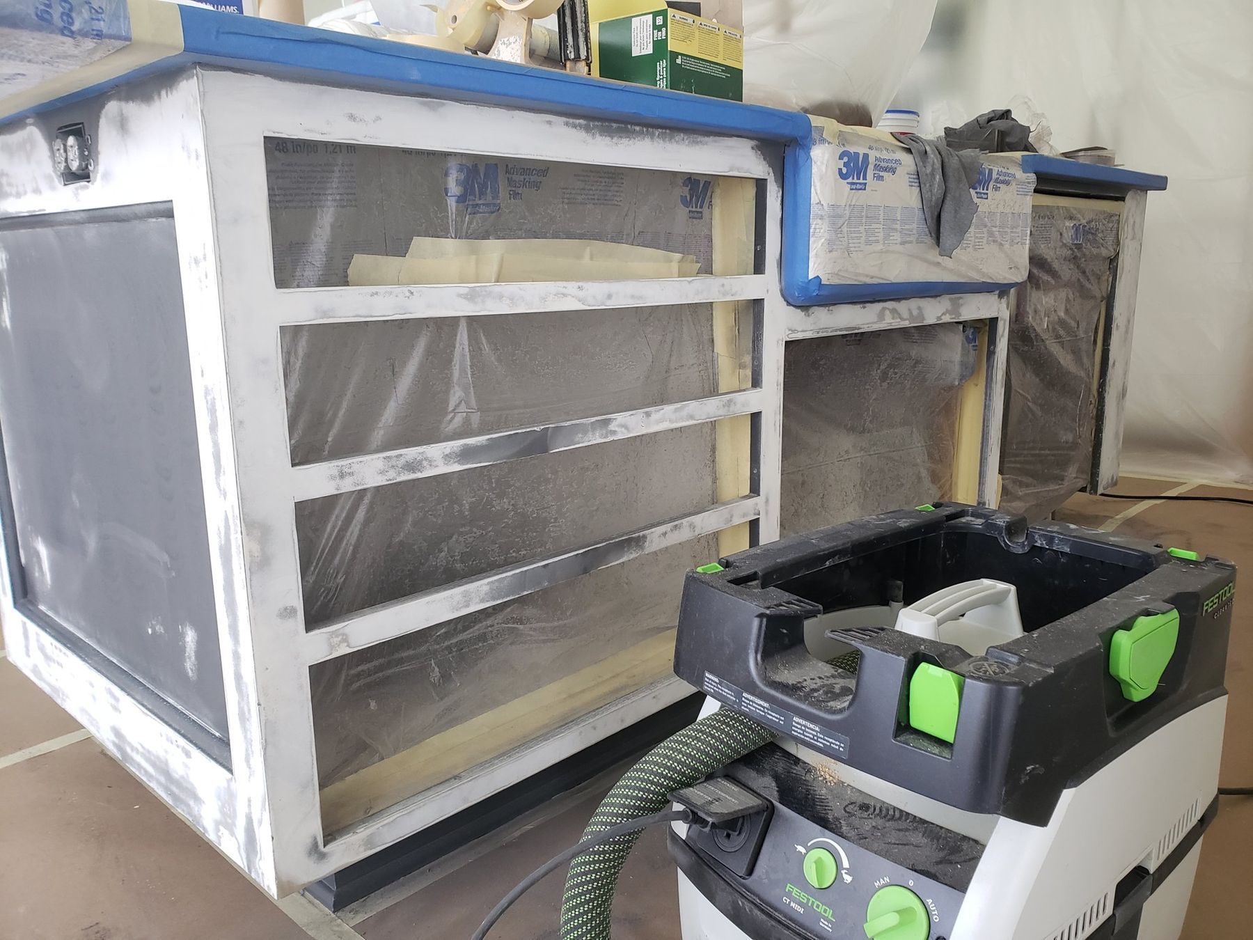 Kitchen island being sanded, masked in plastic, with a dust-extracting vacuum