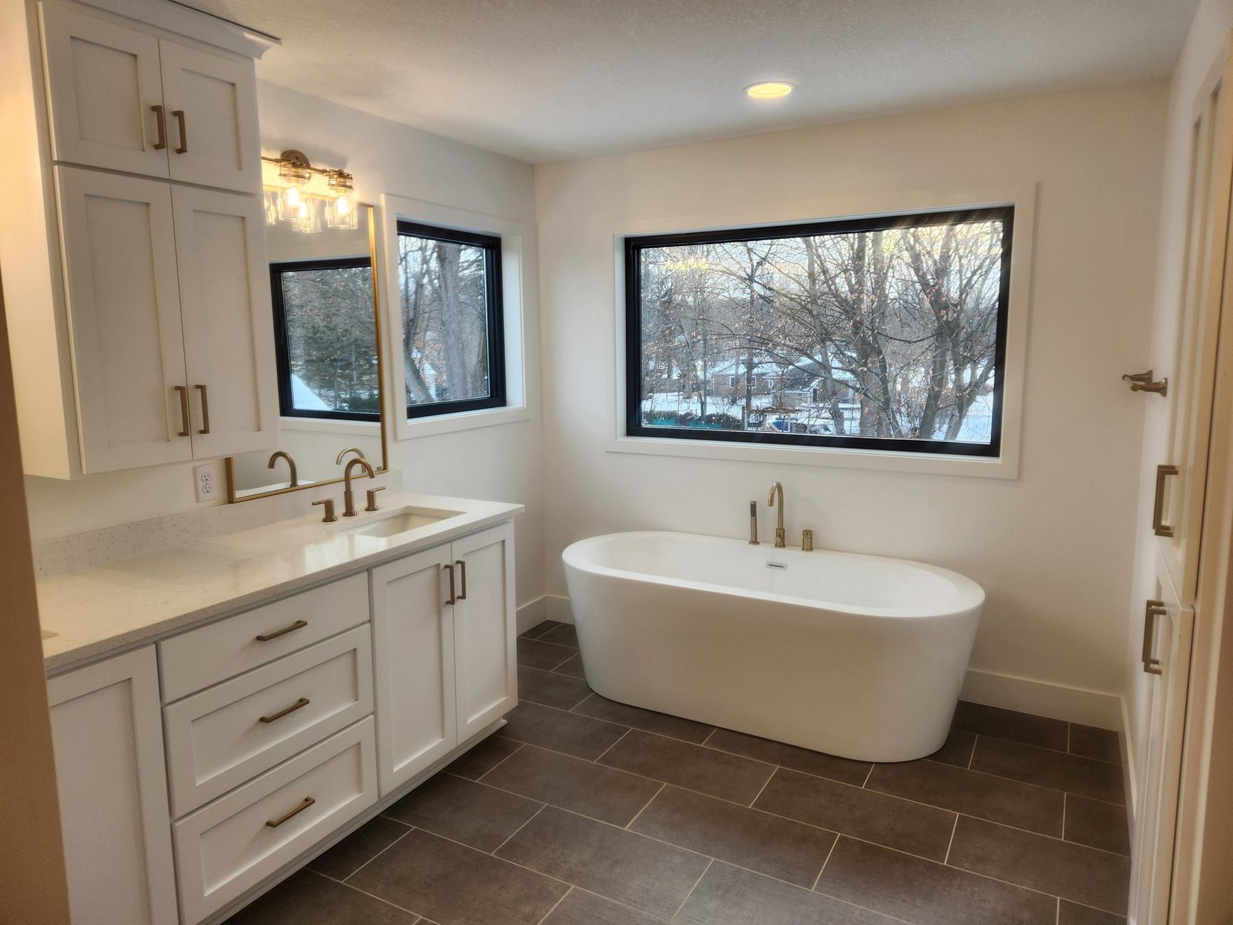 Primary bath with a freestanding tub, white cabinetry and black-framed windows
