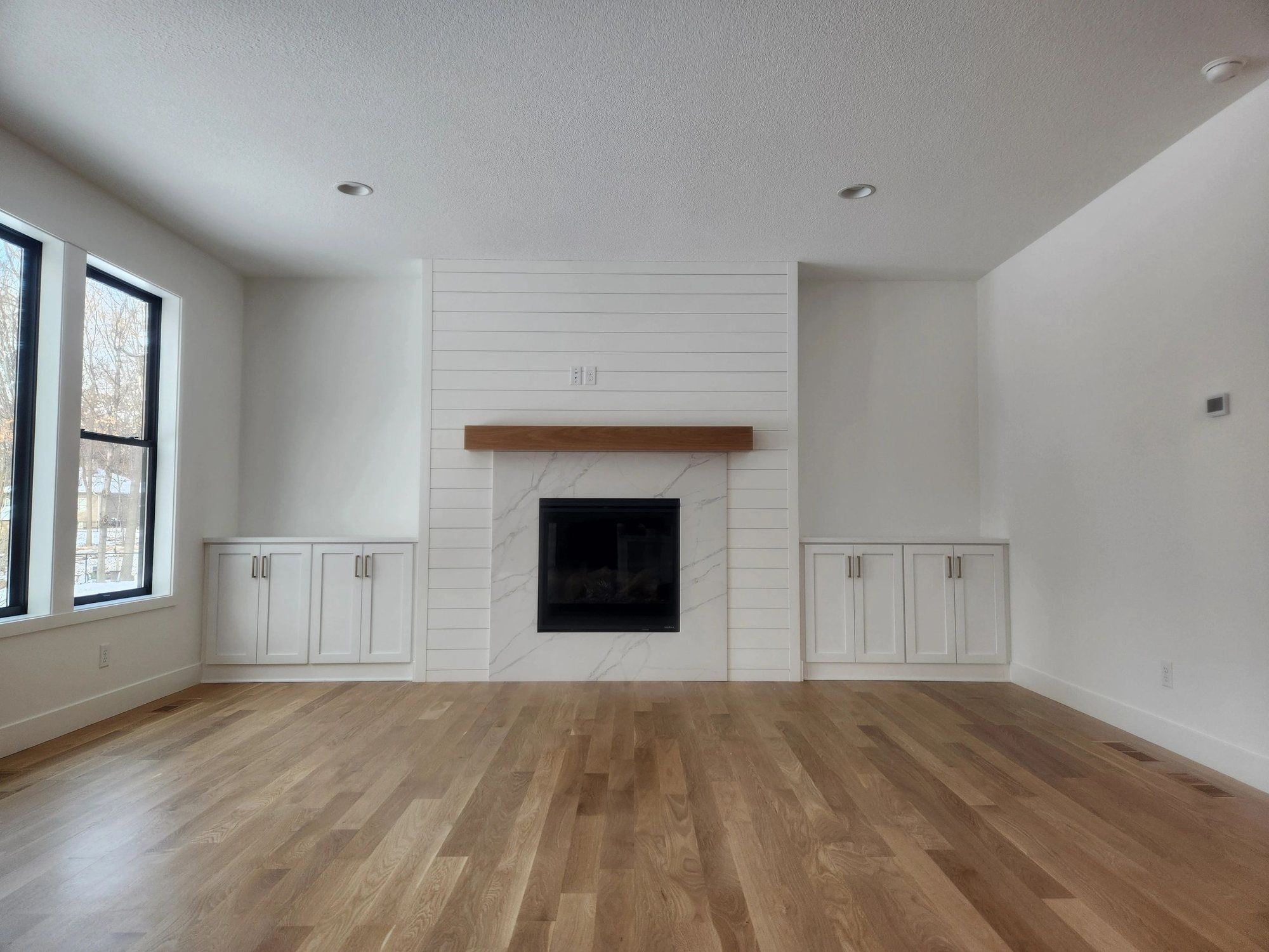 Bright living room with white walls, shiplap fireplace and built-in cabinets