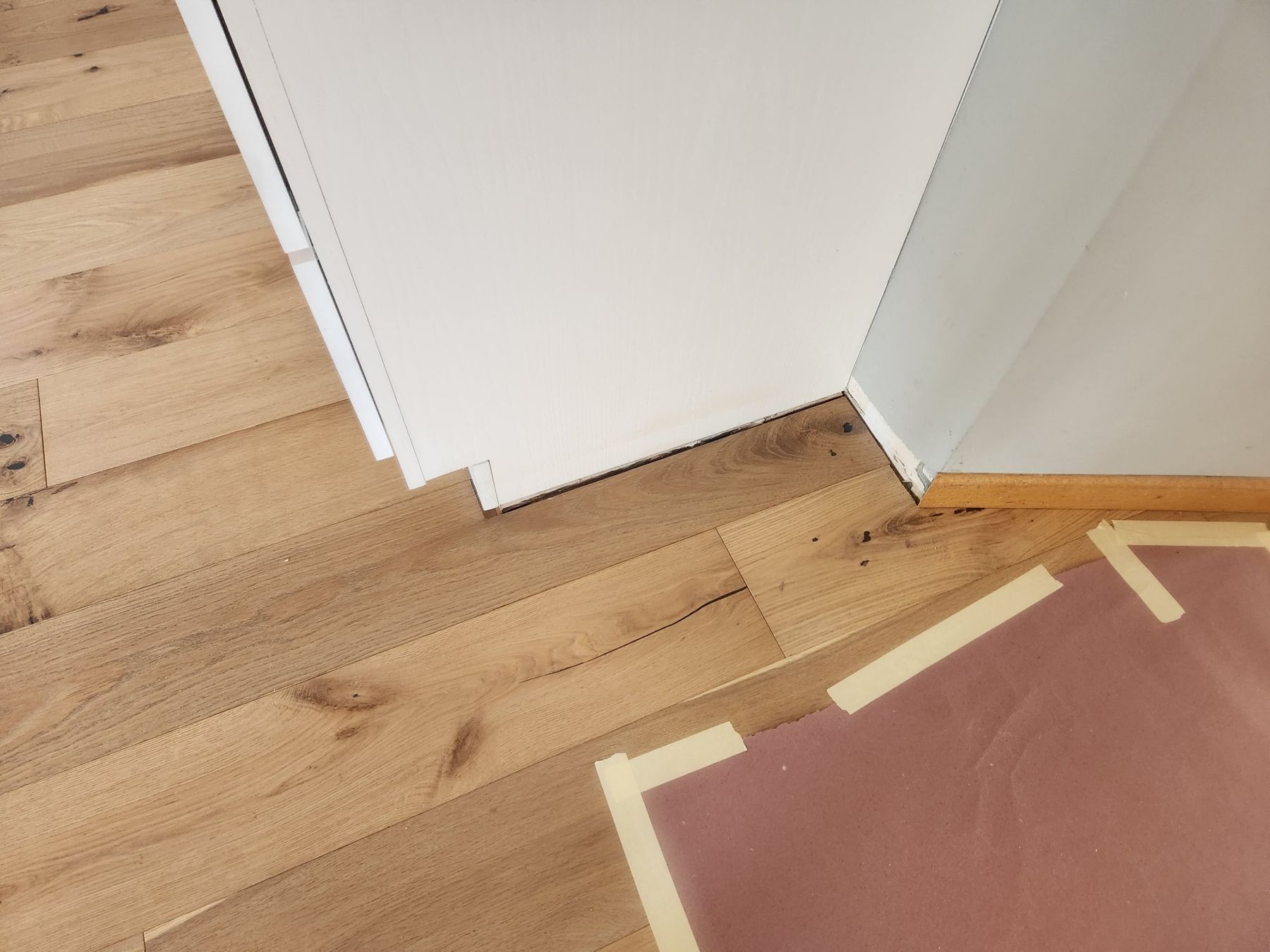 Rosin paper and tape protecting new white-oak floors at a painted corner