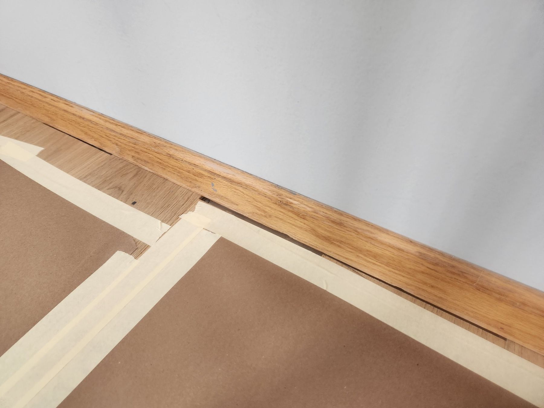 Golden oak baseboard masked for priming, floors papered